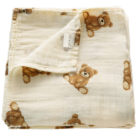 A beige Muslin swaddle blanket with a pattern of teddy bear faces in a repeated design.