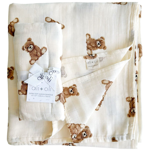 A beige Muslin swaddle blanket with a pattern of teddy bear faces in a repeated design.
