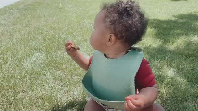 Baby eating pizza with a green silicone bib